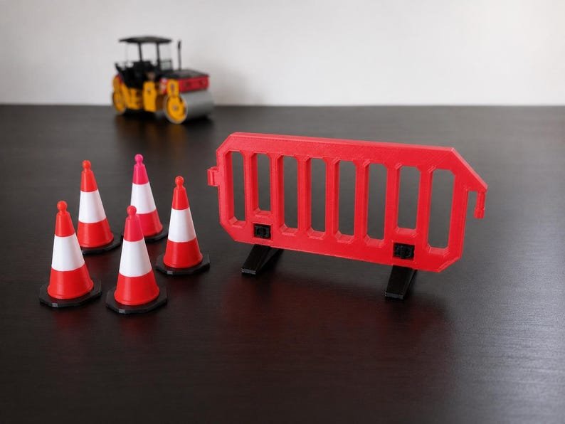 Miniature UK Traffic Cones & Roadwork Barriers Set May include: A set of four miniature orange and white traffic cones, a red plastic construction barrier with black feet, and a yellow and black toy road roller vehicle. The items are arranged together to represent a small construction site scene.