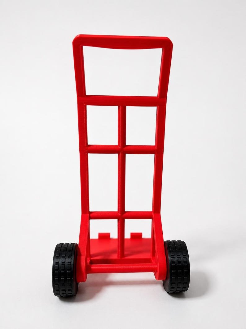 3D Printed Mini Hand Truck Dolly Phone Stand May include: A bright red hand truck featuring a tall, rectangular frame with a central vertical support and a horizontal handle at the top. The base includes a flat platform for loading items, and the unit is supported by two black, textured wheels.