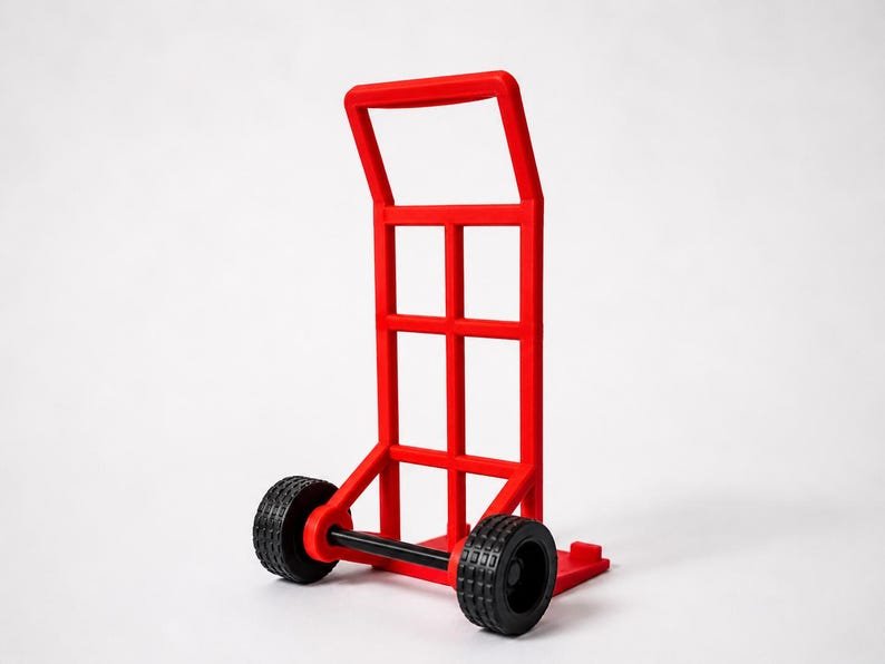 3D Printed Mini Hand Truck Dolly Phone Stand May include: A bright red sack truck featuring a tall, rectangular frame with a grid-like structure, a flat base plate for loading items, and two black wheels with a textured tread pattern connected by a horizontal axle at the bottom.