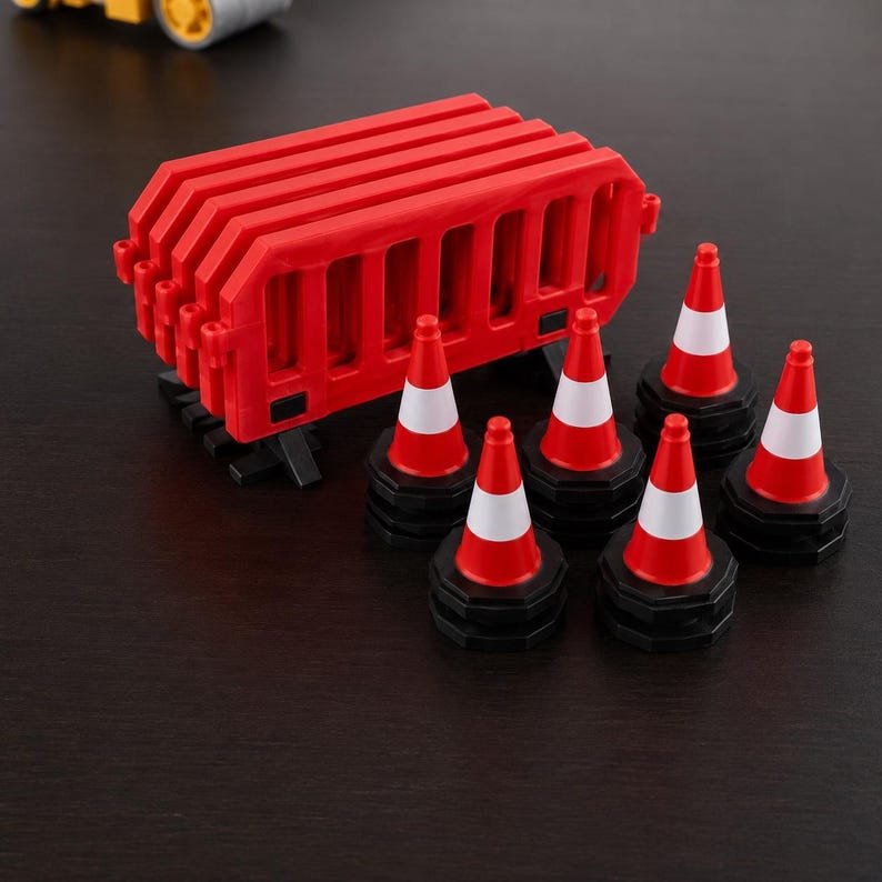 Miniature UK Traffic Cones & Roadwork Barriers Set May include: A set of miniature construction equipment featuring five red plastic safety barriers stacked together and five small traffic cones. Each cone is red with a white horizontal stripe and a black octagonal base for stability.