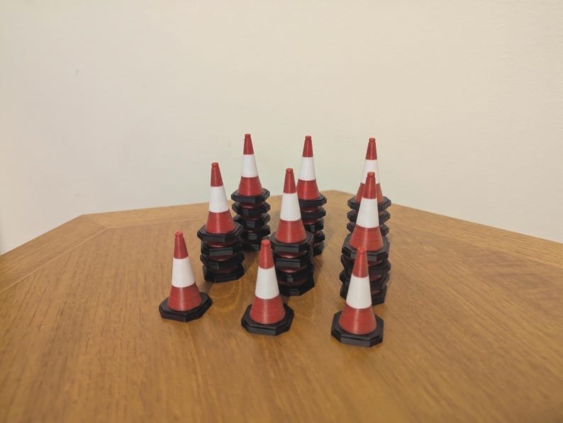 Miniature UK Traffic Cones & Roadwork Barriers Set May include: A collection of miniature traffic cones, each featuring a red and white striped design with a black hexagonal base. These small plastic cones are arranged in several stacks of varying heights, displaying a uniform conical shape.