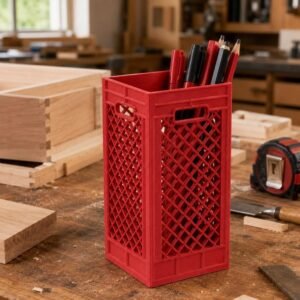 May include: A tall, rectangular red plastic desk organiser designed to resemble a miniature milk crate. The container features a diamond-shaped lattice pattern on all four sides, integrated handles at the top, and holds several pens and pencils.