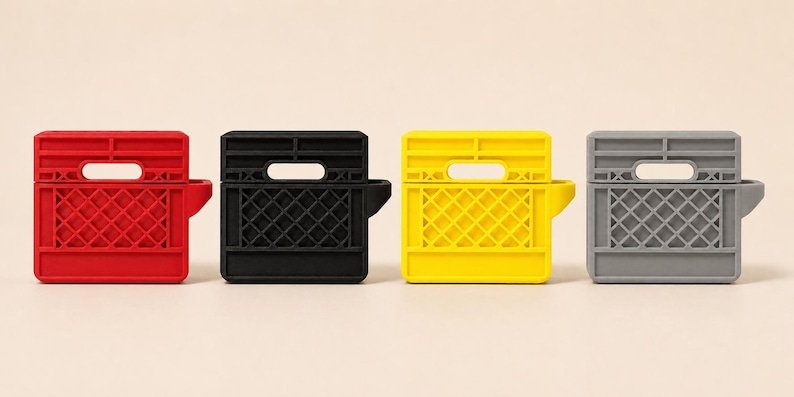 Mini Milk Crate AirPods 4 Case May include: Four silicone protective cases for wireless earbuds, each shaped like a miniature rectangular milk crate. The cases are available in solid red, black, yellow, and grey, featuring a grid-patterned side and a top handle cutout.