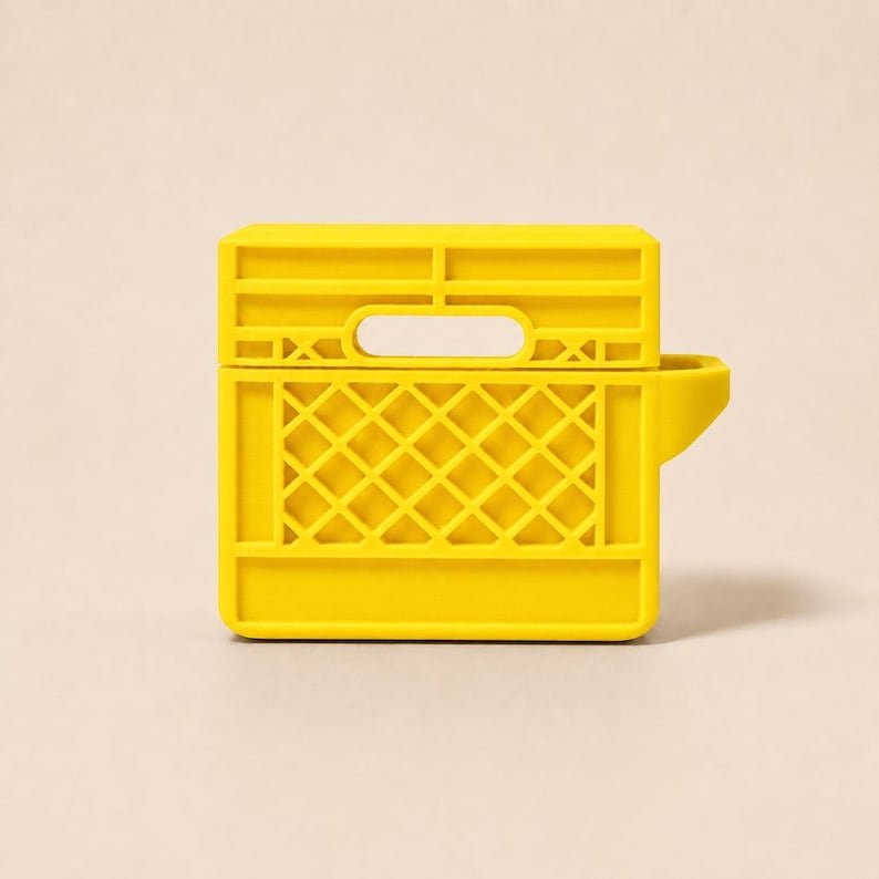 Mini Milk Crate AirPods 4 Case May include: A bright yellow protective case for wireless earbuds, designed to resemble a miniature plastic milk crate. The case features a rectangular shape with a grid-patterned side, a horizontal handle cutout, and a solid base section.