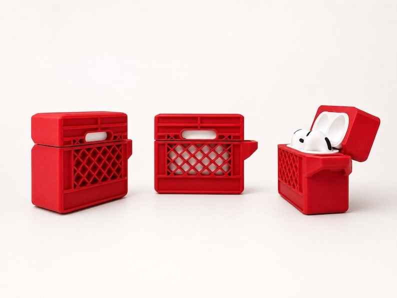 Mini Milk Crate AirPods 4 Case May include: Three red silicone protective cases for wireless earbuds, designed to resemble miniature milk crates. Two cases are closed, while the third is open, revealing white earbud charging components inside the red crate-style housing.