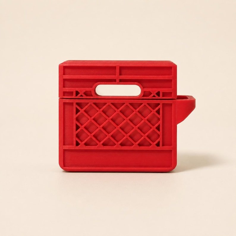 Mini Milk Crate AirPods 4 Case May include: A bright red protective case for wireless earbuds, designed to resemble a miniature plastic milk crate. The case features a rigid, grid-like lattice pattern on the front, a rectangular handle cutout at the top, and a side attachment loop.