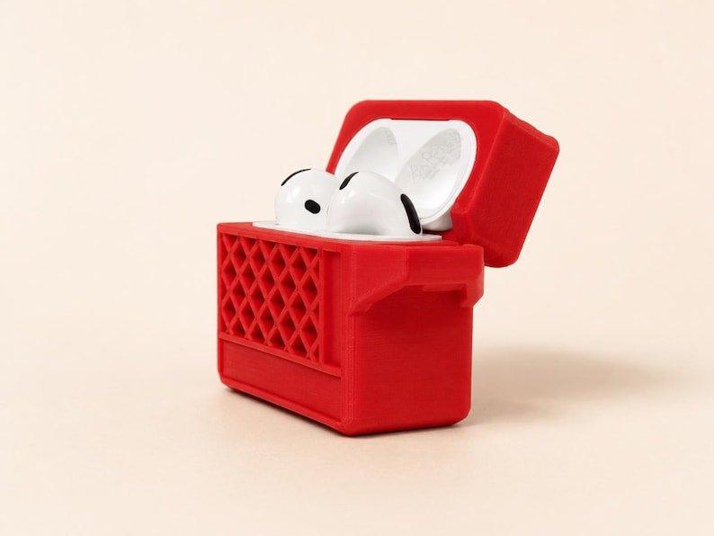 Mini Milk Crate AirPods 4 Case May include: A bright red protective case for wireless earbuds, designed to resemble a small crate with a lattice pattern on the front. The lid is open, revealing a pair of white wireless earbuds nestled inside the rectangular storage compartment.