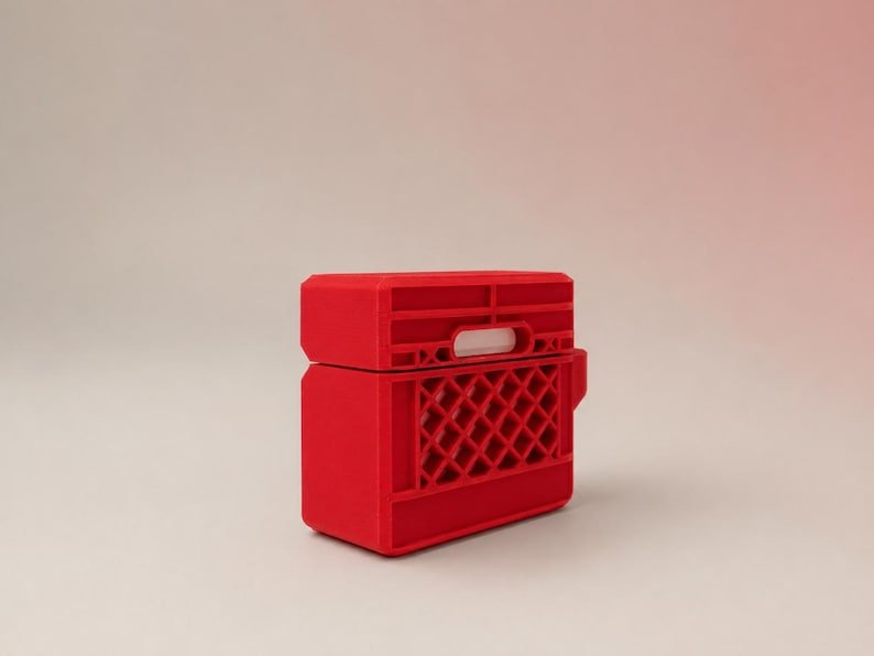 Mini Milk Crate AirPods 4 Case May include: A bright red protective case for wireless earbuds, designed to resemble a miniature plastic milk crate. The case features a rigid, rectangular structure with a grid-like pattern on the sides and a small white rectangular cutout.