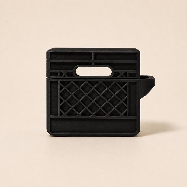 Mini Milk Crate AirPods 4 Case May include: A matte black protective case for wireless earbuds, designed to resemble a miniature plastic milk crate. The case features a rigid, grid-like lattice pattern on the front, a rectangular handle cutout at the top, and a side attachment.