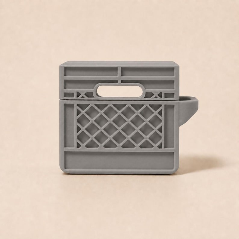 Mini Milk Crate AirPods 4 Case May include: A matte grey silicone protective case for wireless earbuds, designed to resemble a miniature plastic storage crate. The case features a rectangular shape with a grid-patterned side, a top handle cutout, and a side extension for a hinge.
