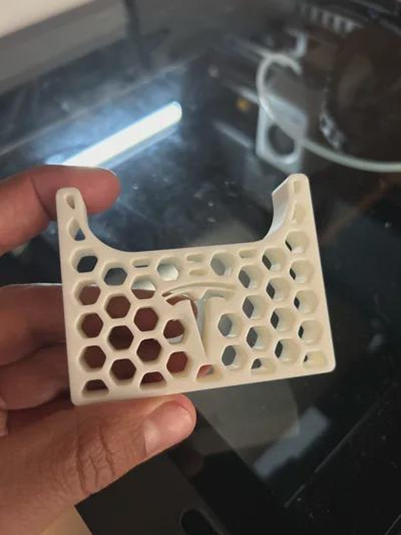 AirPods Pro 2/3 Wireless Charging Spacer for Tesla May include: A white, 3D-printed plastic component featuring a repeating hexagonal honeycomb pattern throughout its rectangular frame. The centre of the piece displays a prominent Tesla logo integrated into the geometric grid structure.
