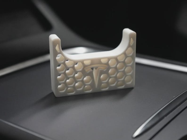 AirPods Pro 2/3 Wireless Charging Spacer for Tesla May include: A white, rectangular, 3D-printed accessory featuring a honeycomb lattice pattern and a central Tesla logo. The object has a U-shaped cutout at the top and a flat base, designed with a geometric, open-frame structure throughout its body.