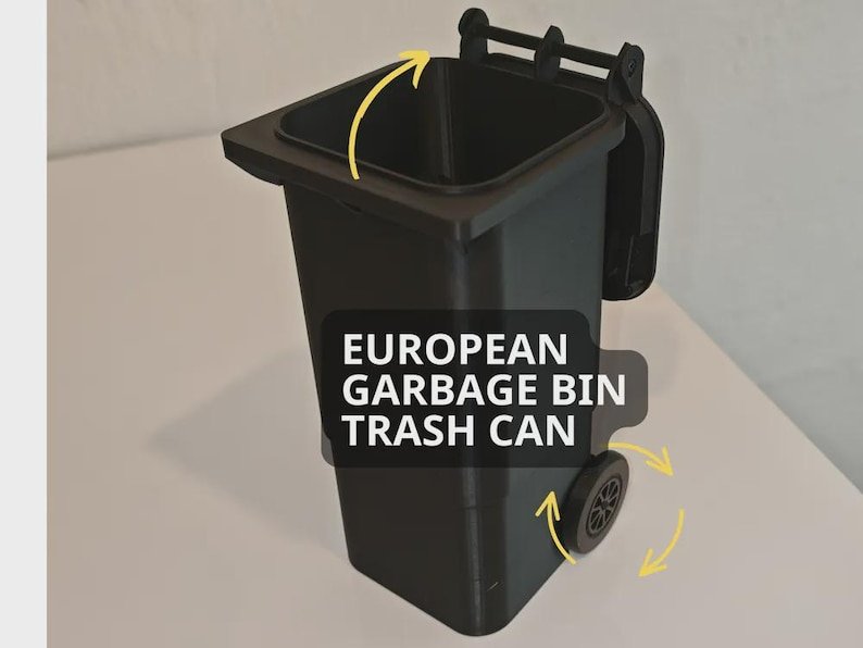 Mini Wheelie Bin Trash Can Pencil Holder May include: A black plastic refuse bin with a hinged lid and two wheels. The text EUROPEAN GARBAGE BIN TRASH CAN is printed on the front. Yellow arrows indicate the movement of the lid and the rotation of the wheels on the side.