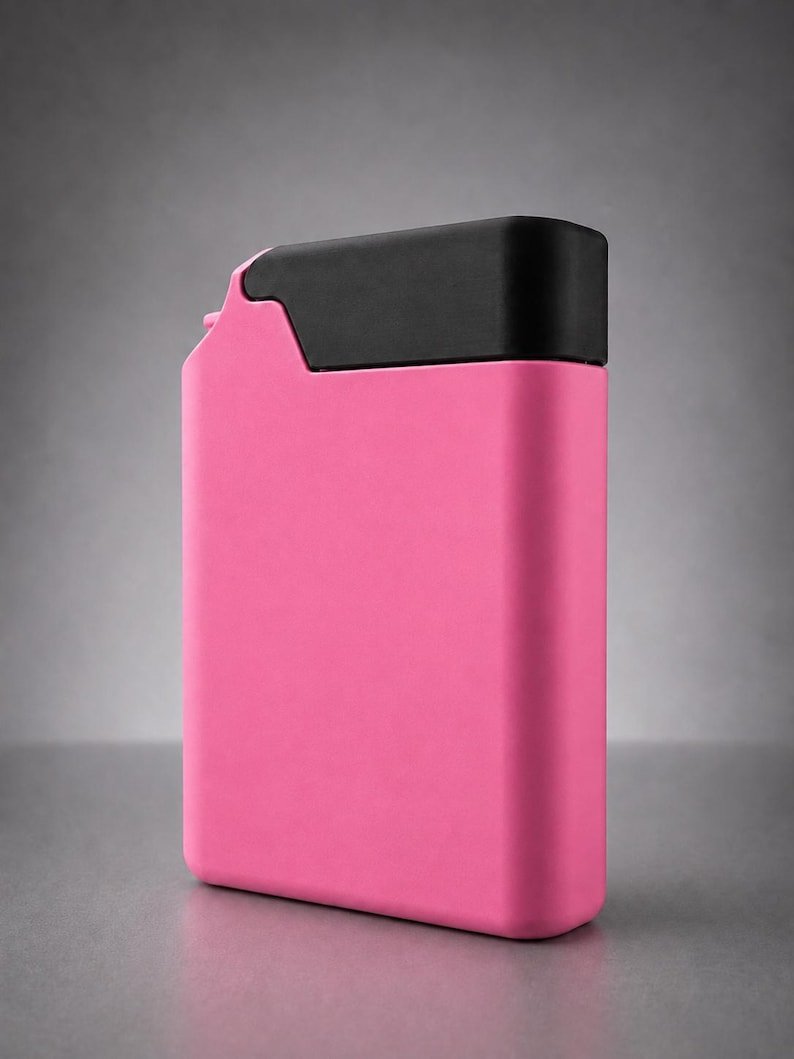 Pink Cigarette Case with Built-In Lighter Holder May include: A rectangular, flat, pink container with a matte finish and a solid black cap covering the top section. The object has a smooth, uniform surface and a distinct, angular shape at the top corner, resembling a slim, portable fuel canister.