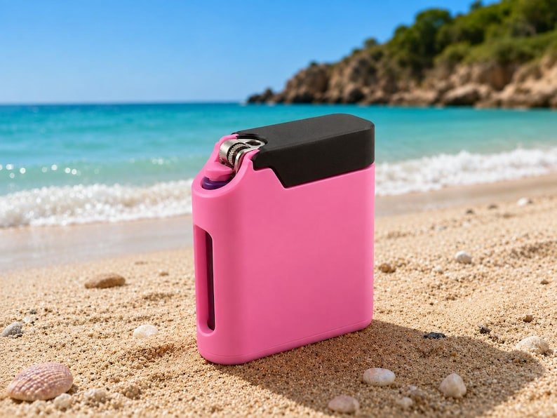 Pink Cigarette Case with Built-In Lighter Holder May include: A rectangular lighter case in a vibrant pink colour with a smooth matte finish. The case features a black top section and a metallic ignition mechanism exposed at the top corner, with a vertical cutout on the side of the pink body.