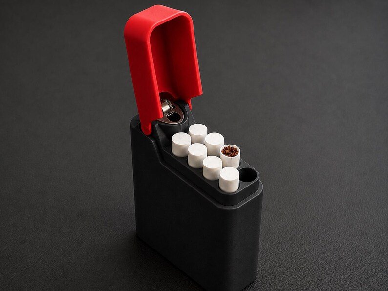 Packout Inspired Cigarette Case (King size / cigarette 8) May include: A black rectangular cigarette case with an integrated red lighter mechanism at the top. The case is open, revealing several white cigarette filters arranged in a grid pattern, with one filter showing brown tobacco contents inside.