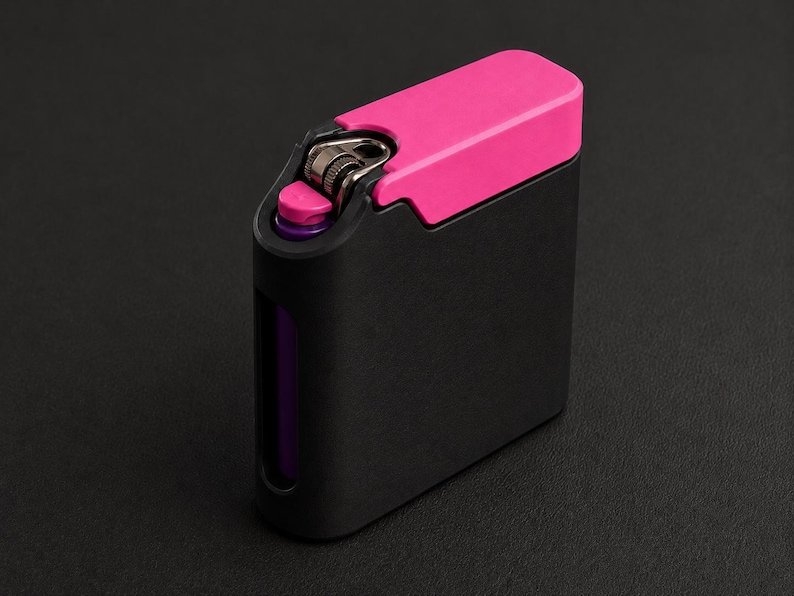Packout Inspired Cigarette Case (King size / cigarette 8) May include: A rectangular lighter case featuring a matte black finish with a vibrant hot pink top cover. The design includes a cutout section on the side revealing a purple inner component, with a metallic ignition mechanism exposed at the top.
