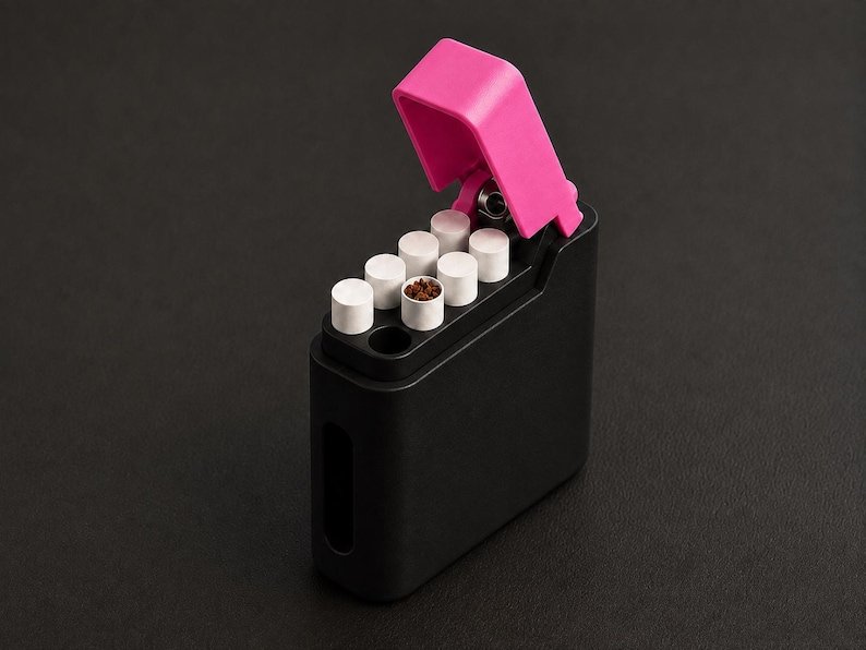 Packout Inspired Cigarette Case (King size / cigarette 8) May include: A black rectangular case with a hinged bright pink lid, containing seven white cylindrical inserts. One insert is open at the top, revealing a brown granular substance inside, while the others are capped with flat white circular tops.
