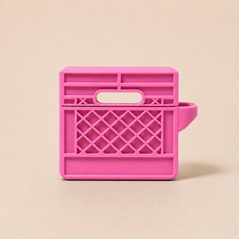 Mini Milk Crate AirPods 4 Case May include: A bright pink silicone protective case for wireless earbuds, designed to resemble a miniature milk crate. The case features a rectangular shape with a grid-like lattice pattern on the front and a small handle cutout at the top.