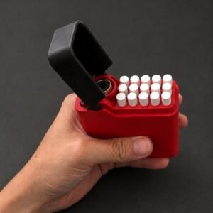 May include: A rectangular red case with a hinged black lid, featuring a grid of fifteen small white cylindrical inserts arranged in three rows of five. The open lid reveals a circular metallic component inside the top section of the red housing.