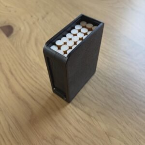 May include: A rectangular black cigarette case with a textured finish, featuring a ribbed side panel and an open top revealing a cluster of white cigarettes with tan filters arranged vertically inside the container.