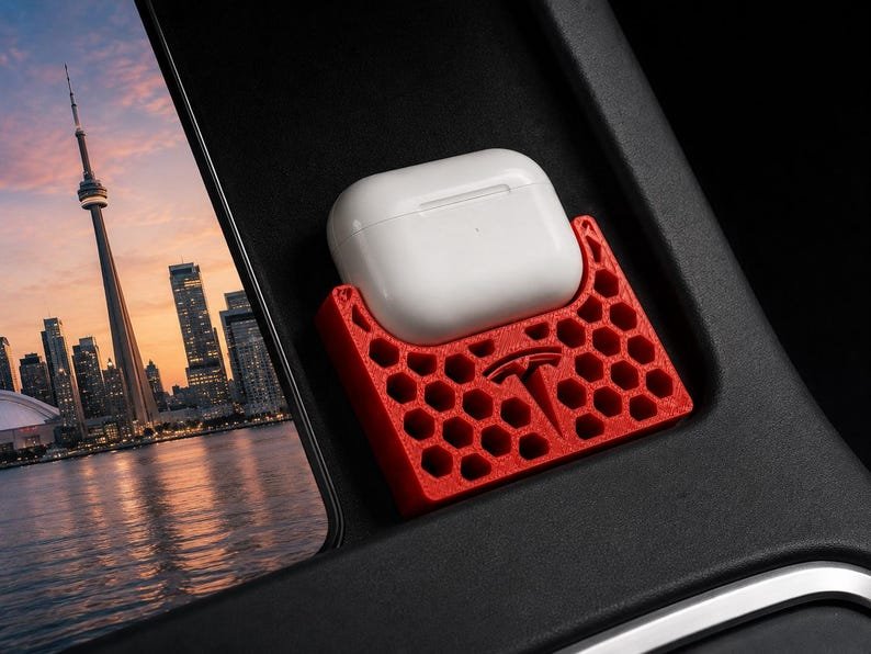AirPods Pro 2/3 Wireless Charging Spacer for Tesla May include: A red 3D-printed honeycomb-patterned storage tray featuring a Tesla logo, designed to hold a white wireless earbud charging case. The tray is positioned within a black automotive console compartment next to a view of a city skyline.