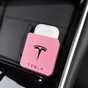 May include: A pink square holder featuring the black Tesla logo and text, designed to fit into a vehicle console. A white wireless earbud charging case is inserted into the top of the holder, which is positioned against a black interior surface.