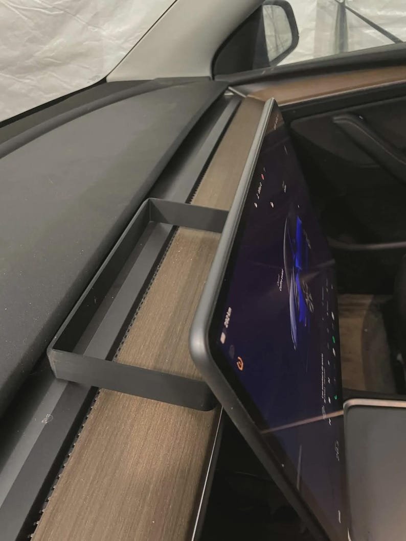 Tesla Model 3 & Model Y Tissue Box Holder May include: A matte black rectangular storage tray designed to sit on the dashboard of a vehicle, positioned directly behind the central touchscreen display. The tray features a low-profile frame and is mounted on the wood-grain dashboard surface.