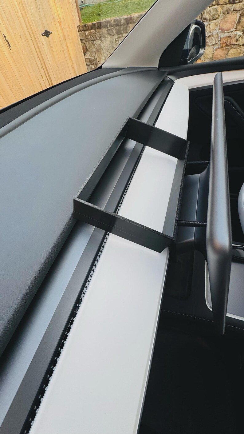 Tesla Model 3 & Model Y Tissue Box Holder May include: A black rectangular storage tray mounted behind the infotainment screen on a vehicle dashboard. The tray features a flat base and raised edges, designed to sit securely on the white dashboard trim panel within the car interior.
