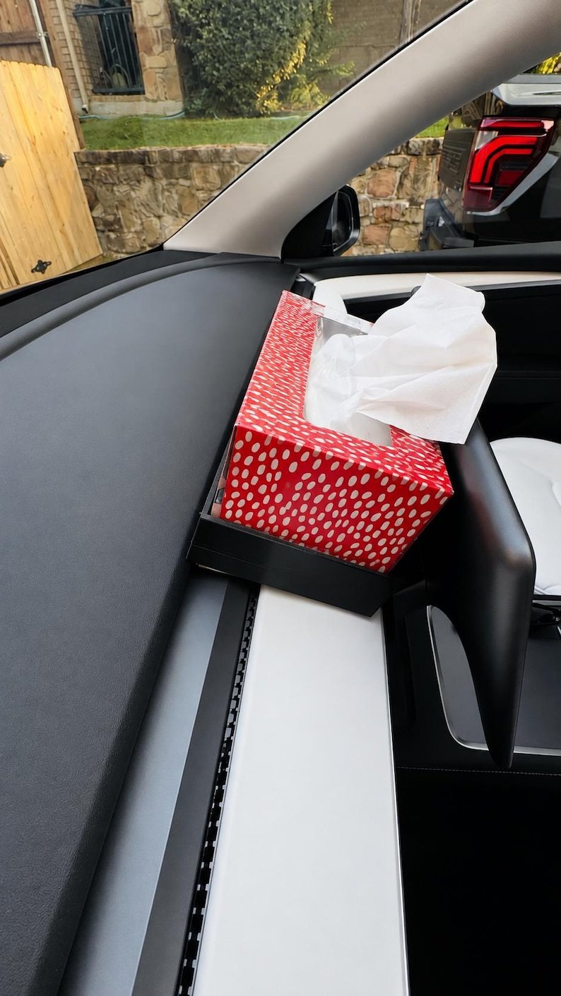 Tesla Model 3 & Model Y Tissue Box Holder May include: A rectangular tissue box holder with a vibrant red exterior featuring a white polka dot pattern. The holder is mounted on the dashboard of a vehicle and contains a stack of white facial tissues protruding from the top opening.