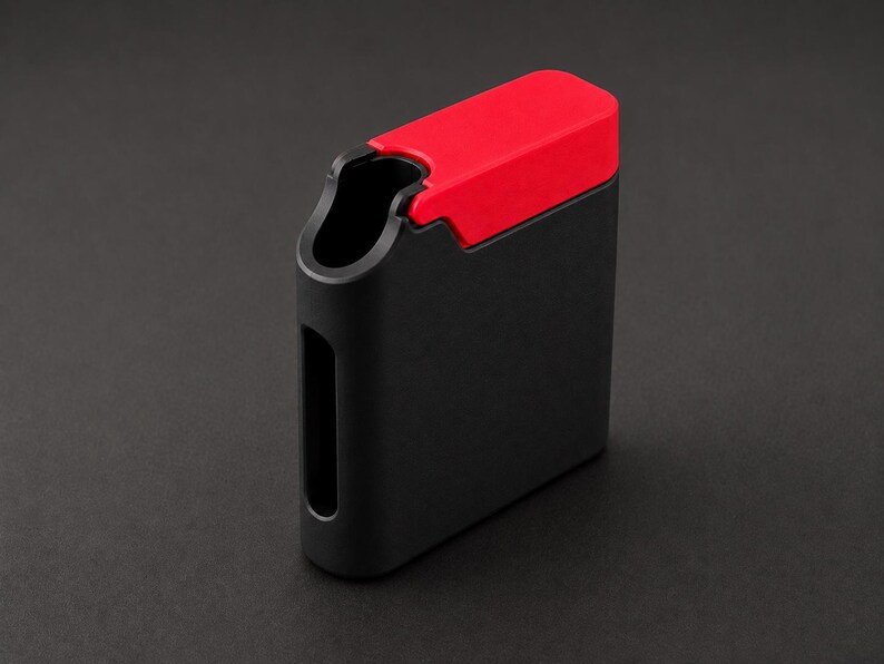 Packout Inspired Cigarette Case (King size / cigarette 8) May include: A rectangular matte black case featuring a vibrant red sliding lid mechanism. The case has a rounded vertical side with a hollow cutout and a smooth, solid body construction, designed with a clean, functional, and geometric aesthetic.