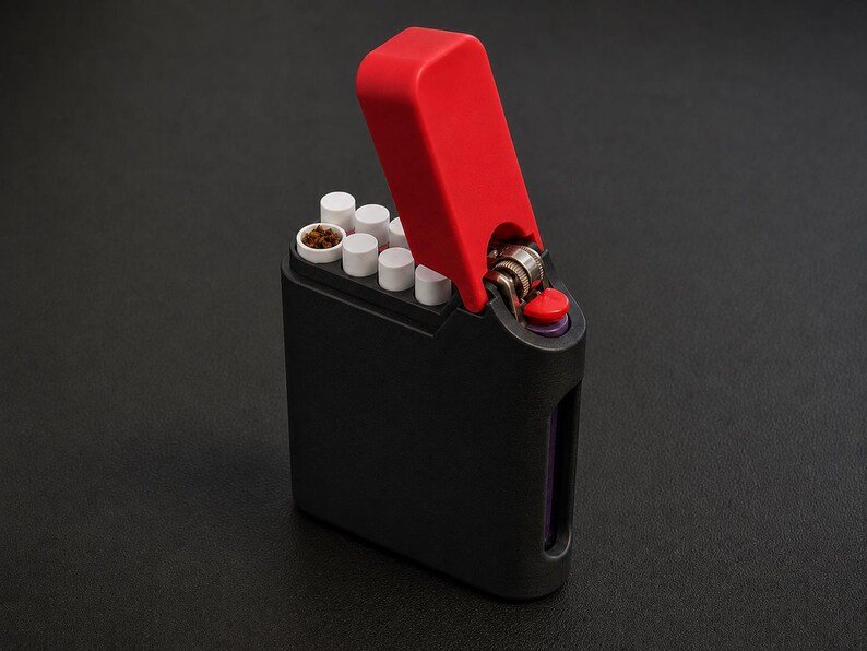 Packout Inspired Cigarette Case (King size / cigarette 8) May include: A black rectangular cigarette case with a red hinged lid. The case holds several white cigarettes with visible tobacco tips. A metal lighter mechanism is integrated into the top right corner of the case, featuring a red ignition button.