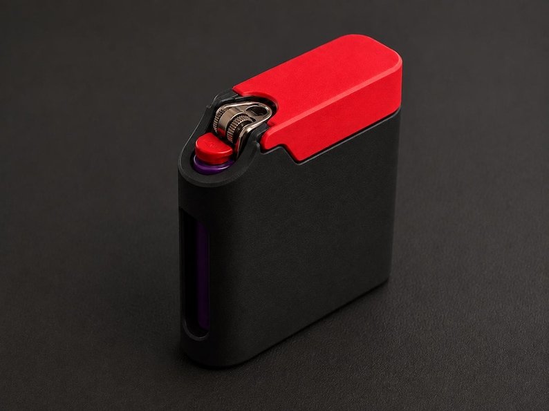 Packout Inspired Cigarette Case (King size / cigarette 8) May include: A rectangular black lighter case with a vibrant red top cover. The case features a cutout section revealing a metallic ignition wheel and a small red button. A purple cylindrical component is visible through a side opening in the frame.