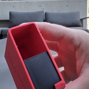 May include: A rectangular red plastic storage container with an open top and a black ribbed insert at the base. The side of the red casing features embossed text that reads Milwaukee, indicating a specialised holder for tools or accessories.