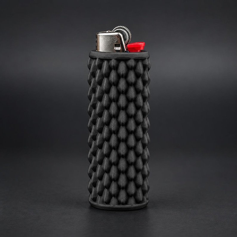 Smooth Dragon Scale BIC Lighter Sleeve May include: A black lighter featuring a cylindrical body with a textured, repeating scale-like pattern. The top mechanism is constructed from silver-toned metal with a small, bright red ignition button positioned on the side of the lighter head.