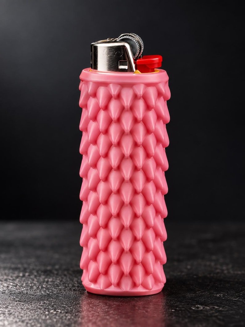 Smooth Dragon Scale BIC Lighter Sleeve May include: A pink lighter featuring a textured, spiked silicone sleeve covering the body. The top of the lighter is made of polished silver metal with a small, bright red ignition button and a dark grey serrated ignition wheel for operation.
