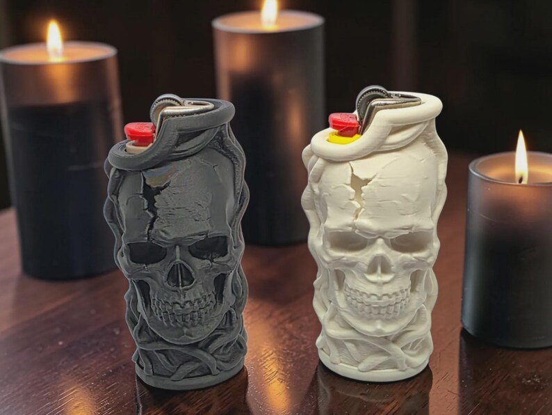 Skull & Roots Lighter Sleeve May include: Two lighter cases, one matte black and one matte white, each featuring a detailed 3D-printed skull design with cracked textures and swirling vine-like patterns. The cases are designed to fit over standard lighters with red ignition buttons.
