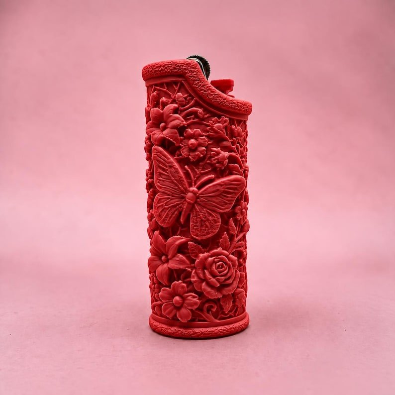 Butterfly Garden Lighter Sleeve May include: A bright red lighter case featuring a detailed, raised relief design of a large butterfly surrounded by various blooming flowers and foliage. The textured surface covers the entire exterior of the cylindrical lighter housing.