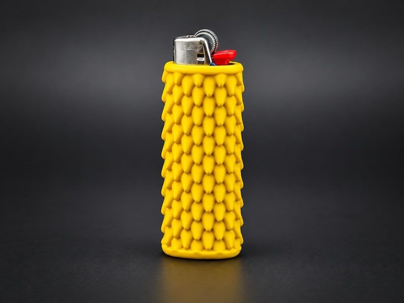 Smooth Dragon Scale BIC Lighter Sleeve May include: A yellow lighter encased in a textured silicone sleeve featuring a repeating pattern of small, pointed, cone-shaped spikes. The top of the lighter displays a metallic ignition mechanism with a small red plastic lever for operation.