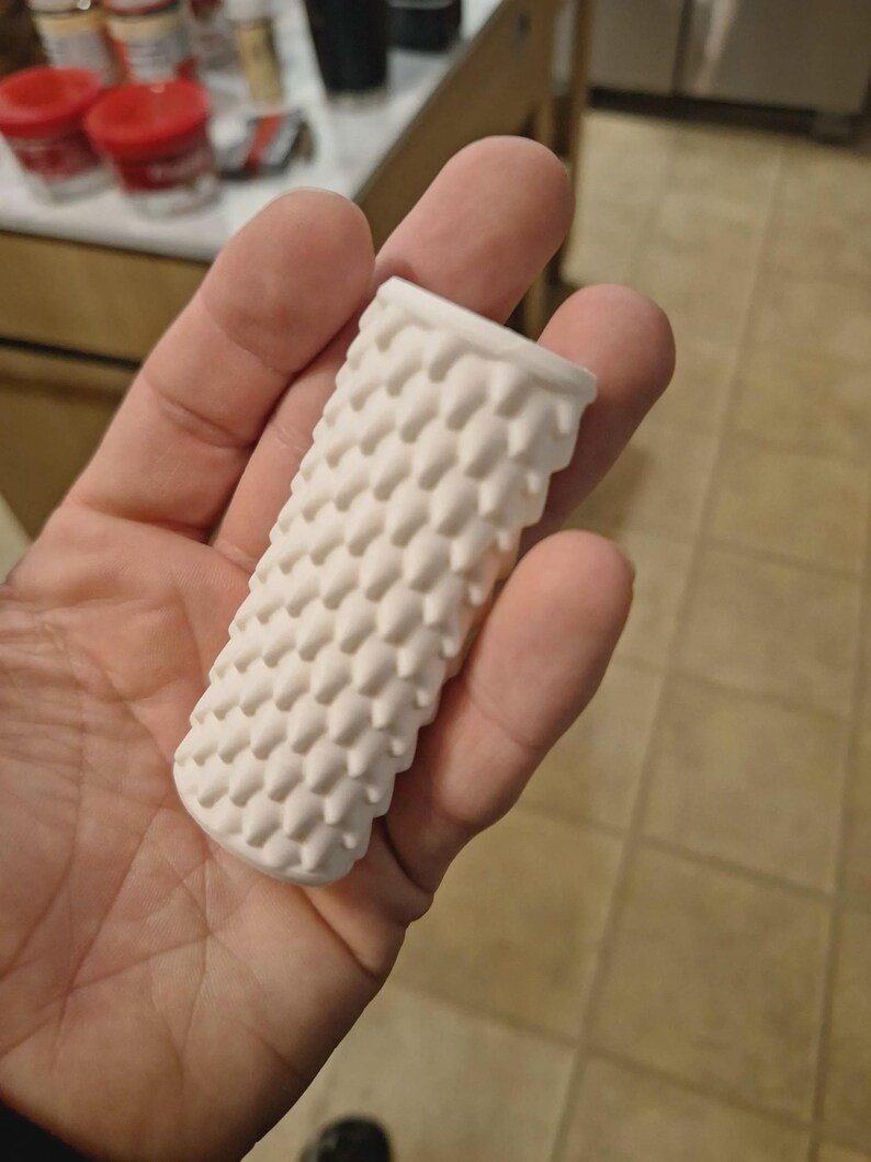Smooth Dragon Scale BIC Lighter Sleeve May include: A cylindrical white object with a textured surface featuring a repeating pattern of small, raised, pointed spikes. The object is hollow and open at one end, with a uniform matte finish across its entire exterior structure.