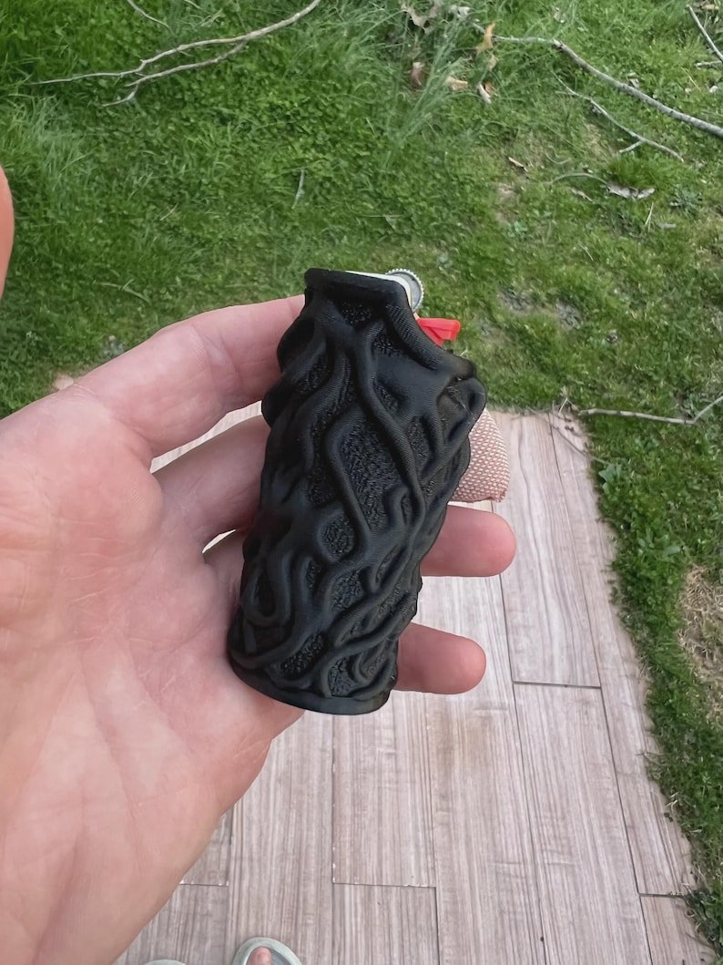 Skull & Roots Lighter Sleeve May include: A black lighter case featuring a raised, organic, root-like or vein-like texture covering the entire exterior surface. The case is designed to fit around a standard rectangular lighter, with the red ignition button visible at the top.