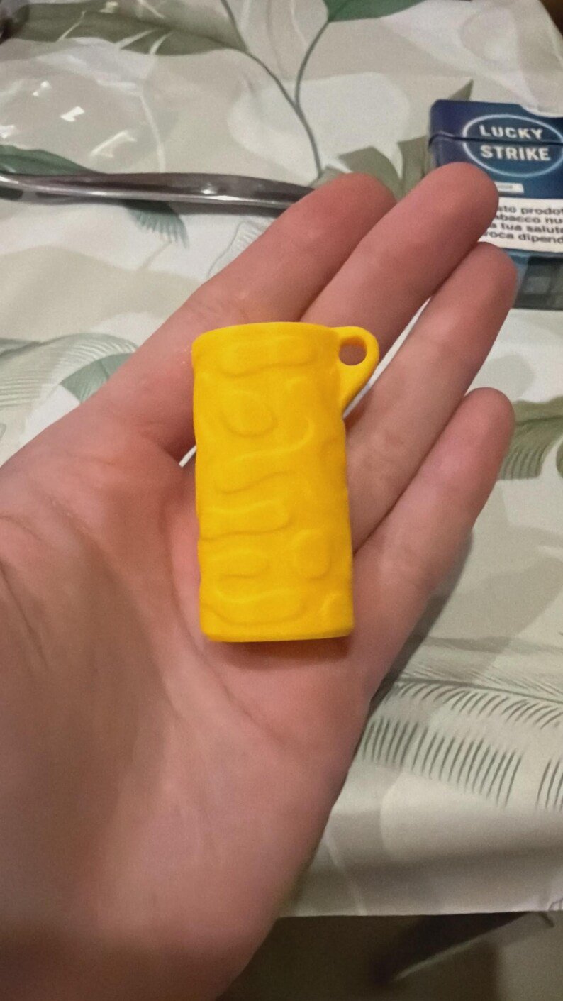 BIC Lighter Keychain Sleeve May include: A bright yellow, cylindrical lighter sleeve featuring a raised, organic, wavy texture across its surface. The sleeve includes a small, circular loop at the top corner for attachment, designed to fit standard rectangular lighters.