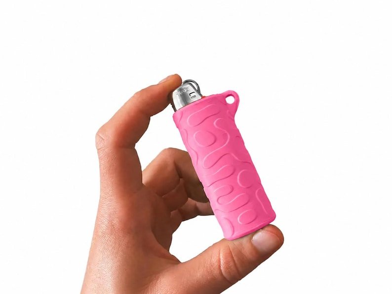 BIC Lighter Keychain Sleeve May include: A bright pink lighter case featuring a raised, wavy, organic pattern across its surface. The case is constructed from a flexible material and includes a small circular loop at the top, designed to fit around a standard rectangular lighter.